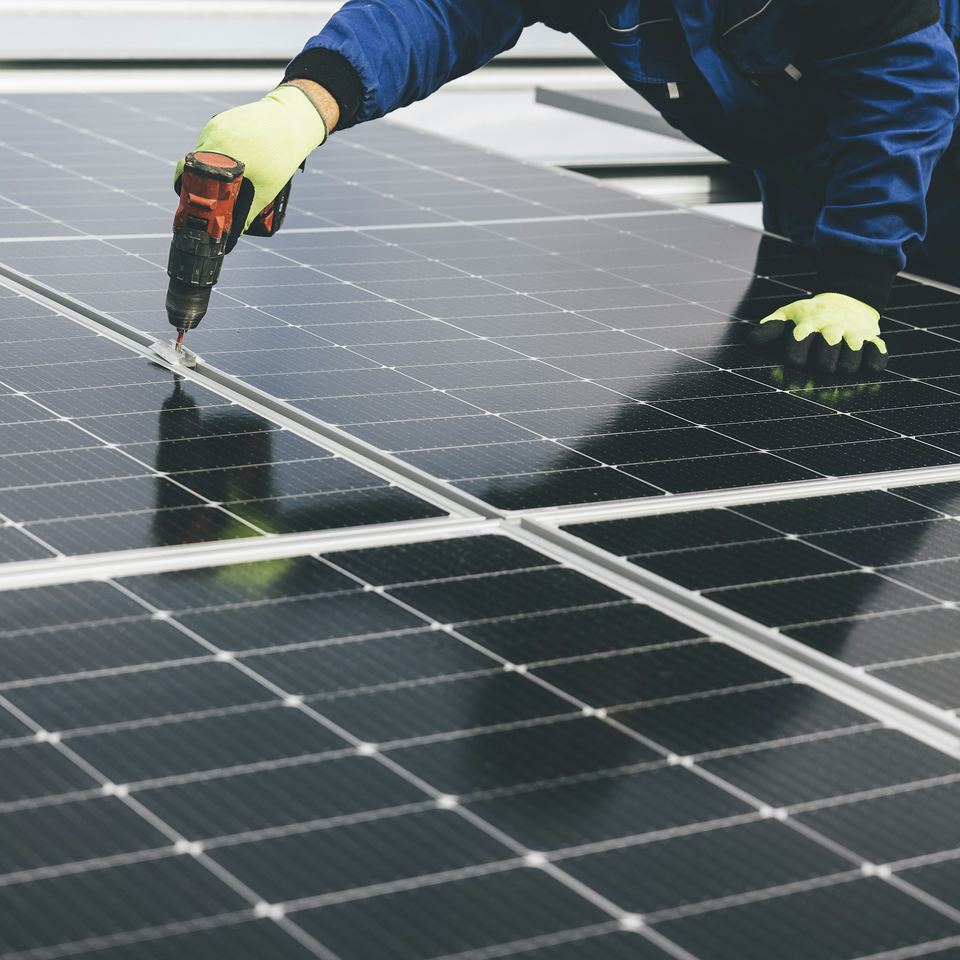A gloved hand using a cordless drill to fix a solar panel to its mounting rail