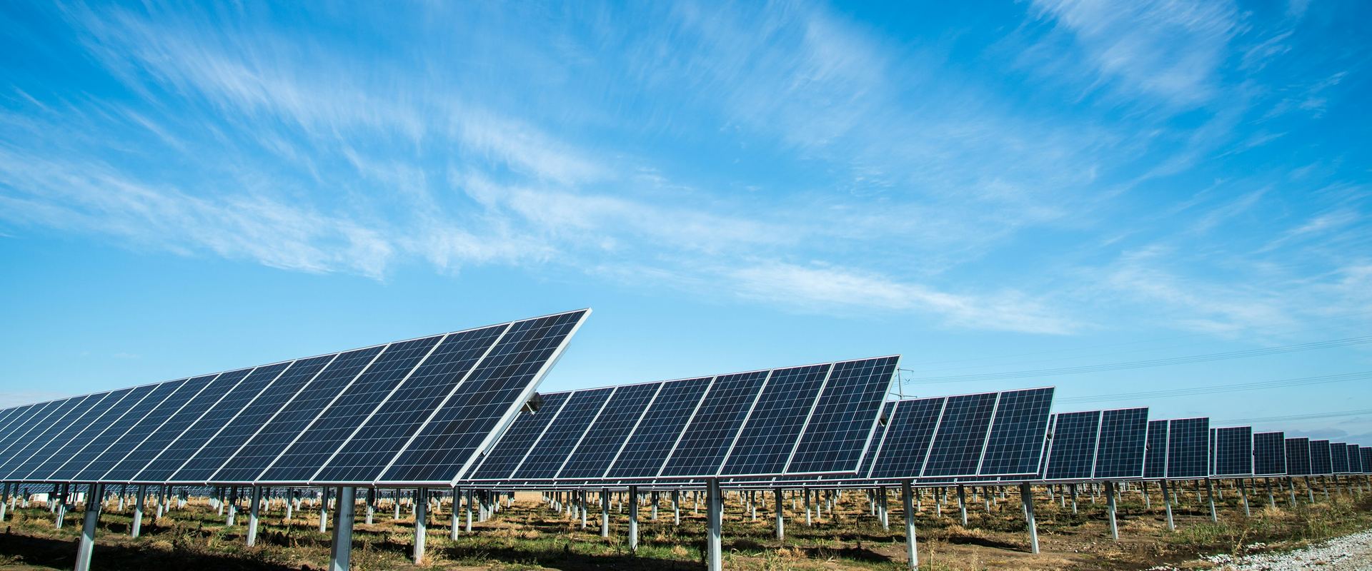 Ground-mounted solar panels beneath a bright blue sky with wispy clouds