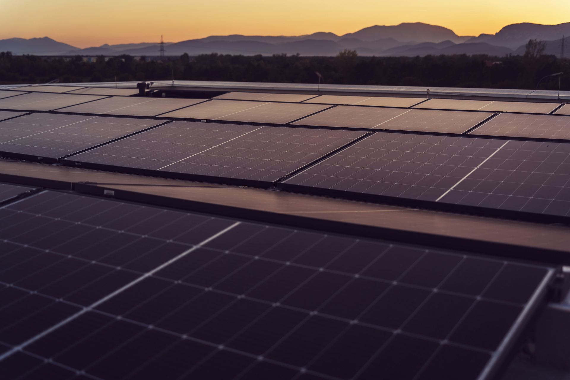 Rows of rooftop solar panels at dusk, with mountains on the horizon