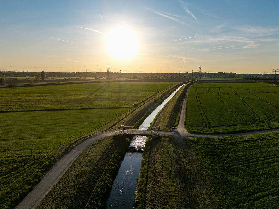 A straight drainage canal running between green fields towards the setting sun